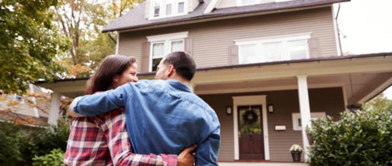 A couple hugs in front of a home.
